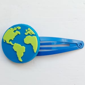 May include: A blue plastic hair clip with a green and blue globe design.