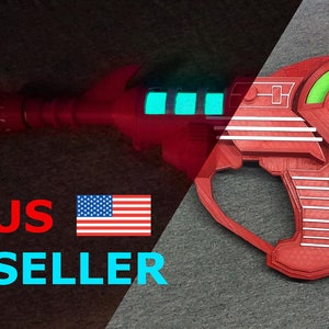 May include: A red toy ray gun with white detailing and a green circular element. The ray gun features a long barrel and a handle. The text "Blast O Matic" is visible on the green circle. The ray gun has glowing blue lights.