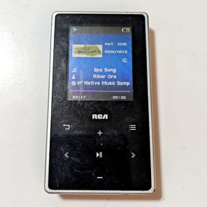 May include: Black RCA MP3 player with a silver frame. The screen displays song information, including "Spa Song" and "Riber Ore." The player has control buttons and a battery indicator. The screen shows 02:17 and 05:20.