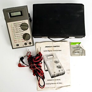 May include: A gray and white Micronta LCD digital multimeter with a black carrying case, owner's manual, and fuses. The multimeter has a digital display and multiple dials and ports. Red and black test leads are also included.