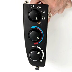 May include: A black automotive climate control panel featuring three circular knobs. The top knob adjusts airflow direction, the middle knob controls temperature with blue and red indicators, and the bottom knob manages fan speed with an OFF setting.