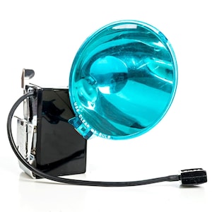 May include: Vintage black camera flash with a bright blue reflector. The flash unit has a rectangular body, a silver-colored mounting bracket, and a black cable with a connector. The reflector has the text "USE CLEAR MS BULB".