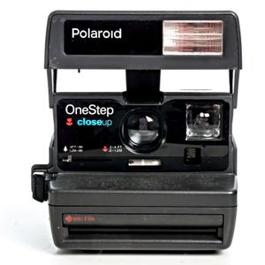 May include: A black Polaroid OneStep closeup instant camera featuring a built-in flash, a central lens, and a viewfinder. The front panel displays the text Polaroid, OneStep closeup, and 600 Film, with focus distance settings of 4FT-infinity and 2-4FT.