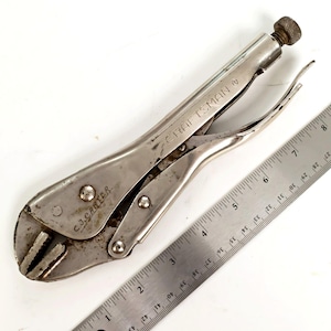 May include: A silver-toned metal locking pliers tool with the brand name CRAFTSMAN and the name C.J. CARTER engraved on the handle. The tool is positioned next to a metal ruler, showing a total length of approximately 8.5 inches.