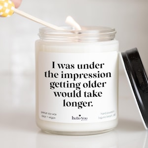 May include: A white candle with a black label that reads "I was under the impression getting older would take longer." The candle is made with premium soy wax and is clean and vegan. The candle is hand-poured in Laguna Beach, California.