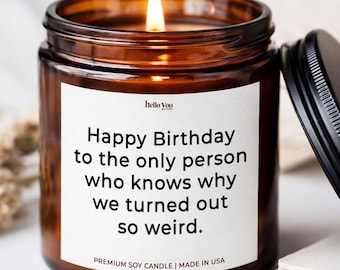 May include: A lit soy candle in an amber glass jar with a black lid. The white label features the text: hello You, Happy Birthday to the only person who knows why we turned out so weird. PREMIUM SOY CANDLE | MADE IN USA.