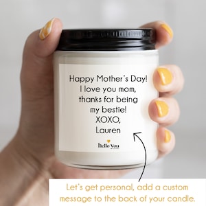 May include: A white candle with a black lid and a personalized message that reads "Happy Mother's Day! I love you mom, thanks for being my bestie! XOXO, Lauren". The candle is in a hand and the text "Let's get personal, add a custom message to the back of your candle." is at the bottom of the image.