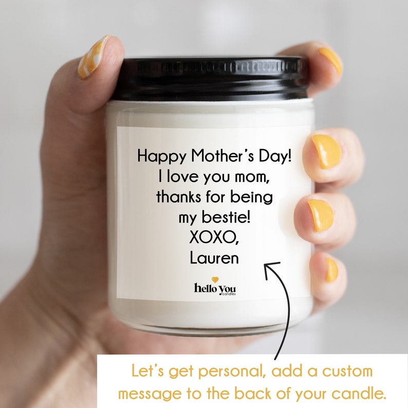 May include: A white candle with a black lid and a personalized message that reads "Happy Mother's Day! I love you mom, thanks for being my bestie! XOXO, Lauren". The candle is in a hand and the text "Let's get personal, add a custom message to the back of your candle." is at the bottom of the image.