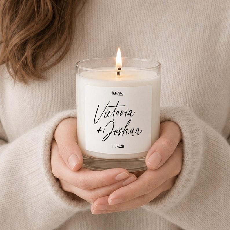 A person's hands holding a lit candle with a label that says "Victoria + Joshua 11.14.28".