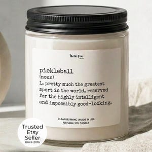 a candle labeled "pickleball" with a definition of the sport, and it is a "clean burning" natural soy candle. The candle is placed on a beige cloth, and there is a "Trusted Etsy Seller since 2016" label at the bottom.