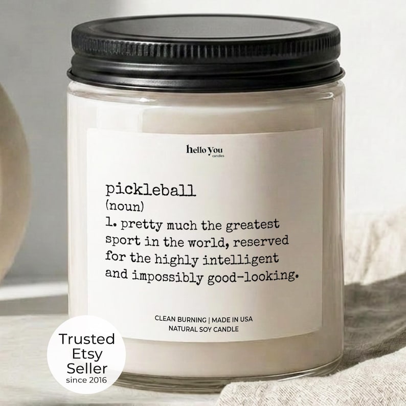 a candle labeled "pickleball" with a definition of the sport, and it is a "clean burning" natural soy candle. The candle is placed on a beige cloth, and there is a "Trusted Etsy Seller since 2016" label at the bottom.