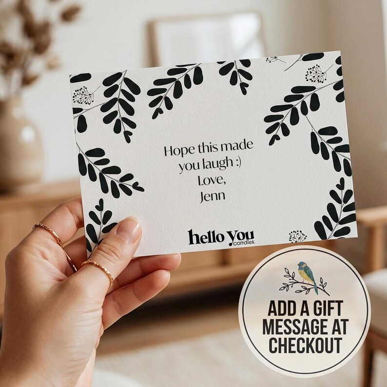 A hand holding a card with a floral design and text, along with a circular sign that reads "ADD A GIFT MESSAGE AT CHECKOUT".