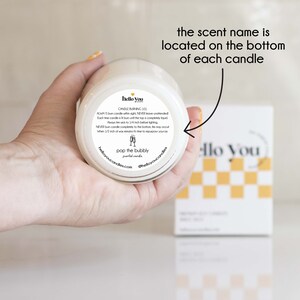 May include: A white candle jar with a black and white label that says "hello you" and "pop the bubbly" scented candles. The label also includes candle burning instructions.