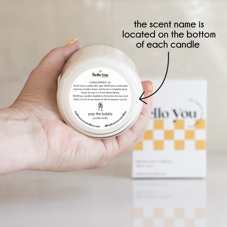 May include: A white candle jar with a black and white label that says "hello you" and "pop the bubbly" scented candles. The label also includes candle burning instructions.