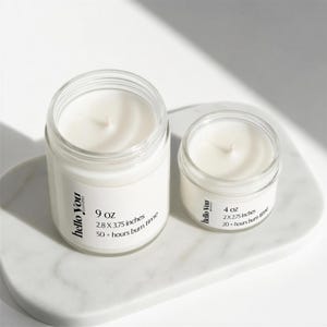 Two candles of different sizes are placed on a white surface, with one candle being larger than the other.