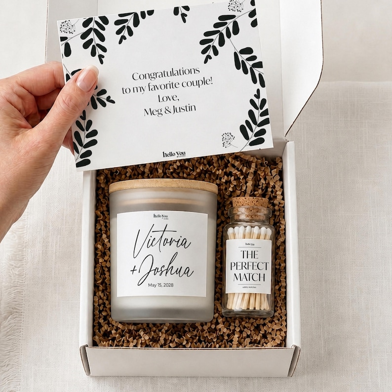 A hand is holding a white box containing a candle and a matchbox, with a card inside the box.