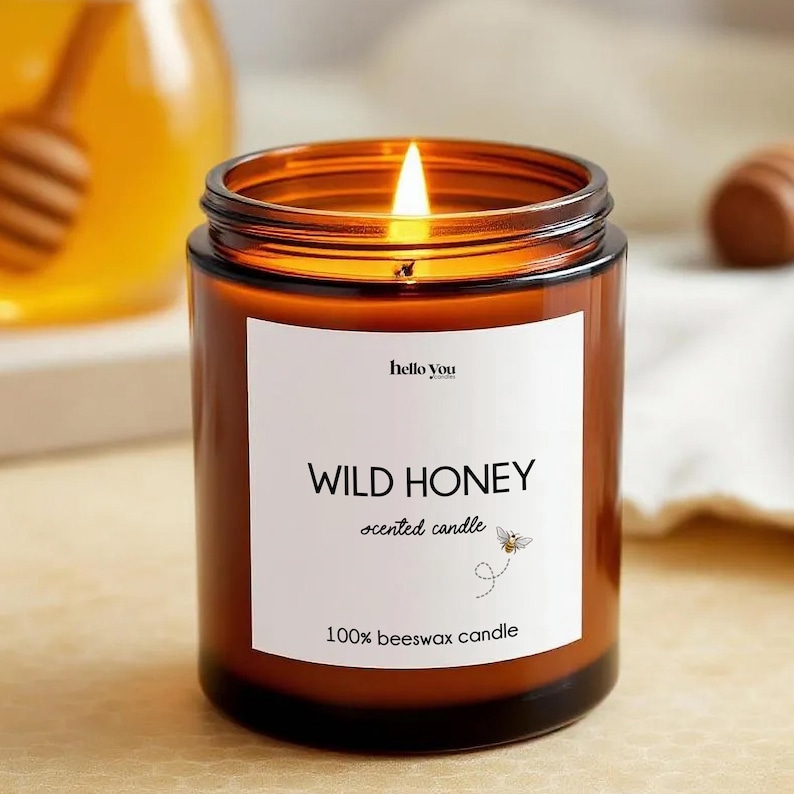 May include: A lit, brown glass jar candle with the text "WILD HONEY scented candle" and "100% beeswax candle" on a white label. A small bee graphic is also on the label. The candle is in focus, with a blurred background.
