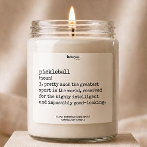 A white candle with a lit wick, accompanied by a label that defines pickleball as "the most intelligent sport in the world, reserved for the highly intelligent and impossible to look at".
