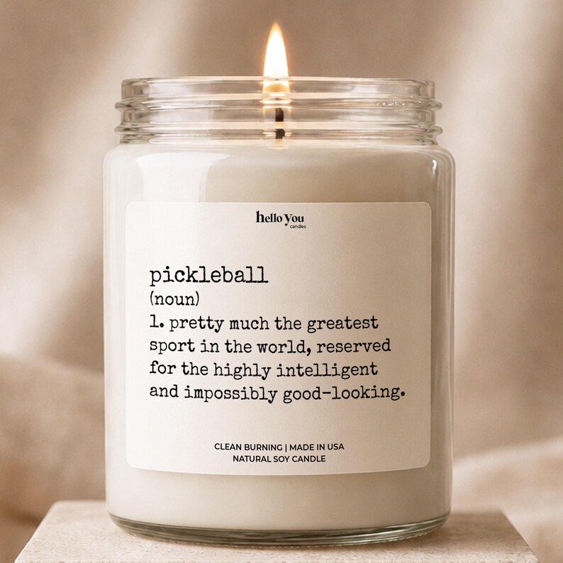 A white candle with a lit wick, accompanied by a label that defines pickleball as "the most intelligent sport in the world, reserved for the highly intelligent and impossible to look at".