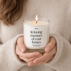 A person's hands holding a lit candle with a label that reads "In loving memory of your forties".