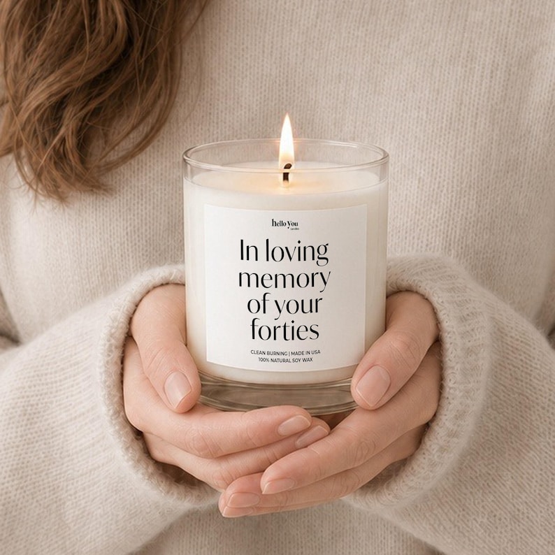 A person's hands holding a lit candle with a label that reads "In loving memory of your forties".