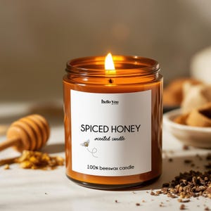 May include: Lit scented candle in a clear glass jar with a white label. The label reads "SPICED HONEY scented candle" with a bee graphic and "100% beeswax candle". The candle is lit with a bright flame.