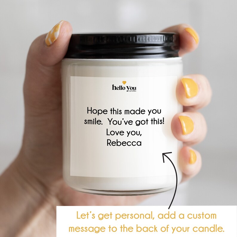 Puede incluir: Una vela blanca con una tapa negra y una etiqueta que dice "hello you candles". La etiqueta tambi&eacute;n tiene un mensaje que dice "Espero que esto te haya hecho sonre&iacute;r. &iexcl;T&uacute; puedes! Te quiero, Rebecca".