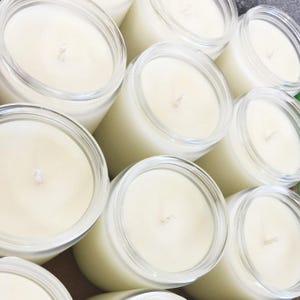 A collection of white candles in clear glass jars, arranged in a grid-like pattern.