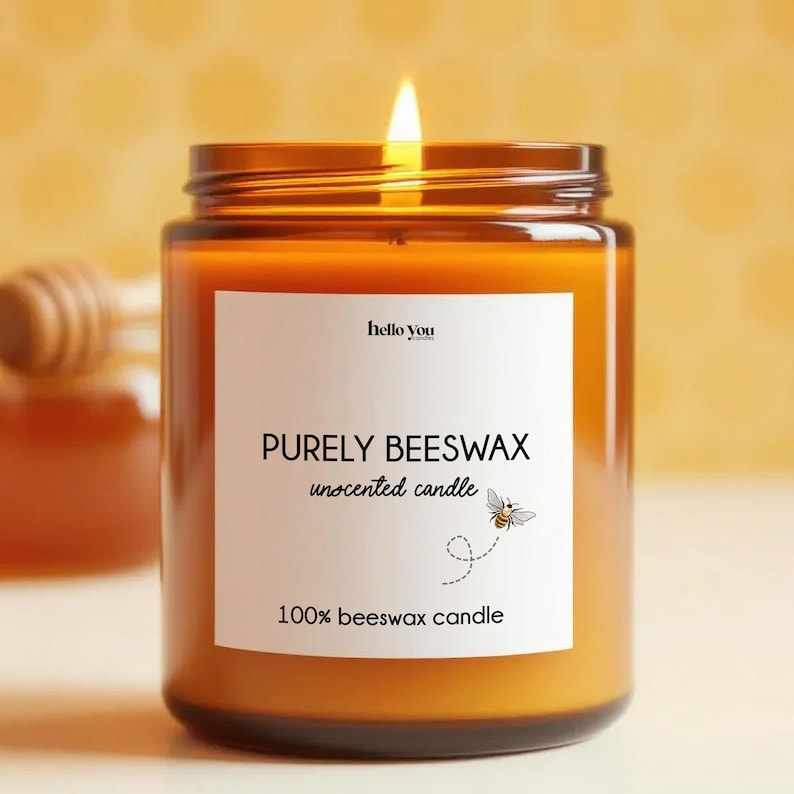 May include: A lit, amber-colored candle in a glass jar. The label reads "PURELY BEESWAX unsented candle" with a bee illustration. The text "100% beeswax candle" is also on the label. The candle is in front of a blurred background.