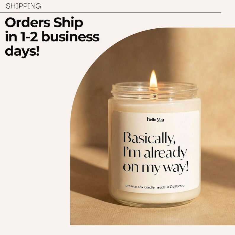 May include: A lit soy candle in a clear glass jar. The candle has a white label with the text "Basically, I'm already on my way!". The text "hello you" is above the main text. The candle is made in California.