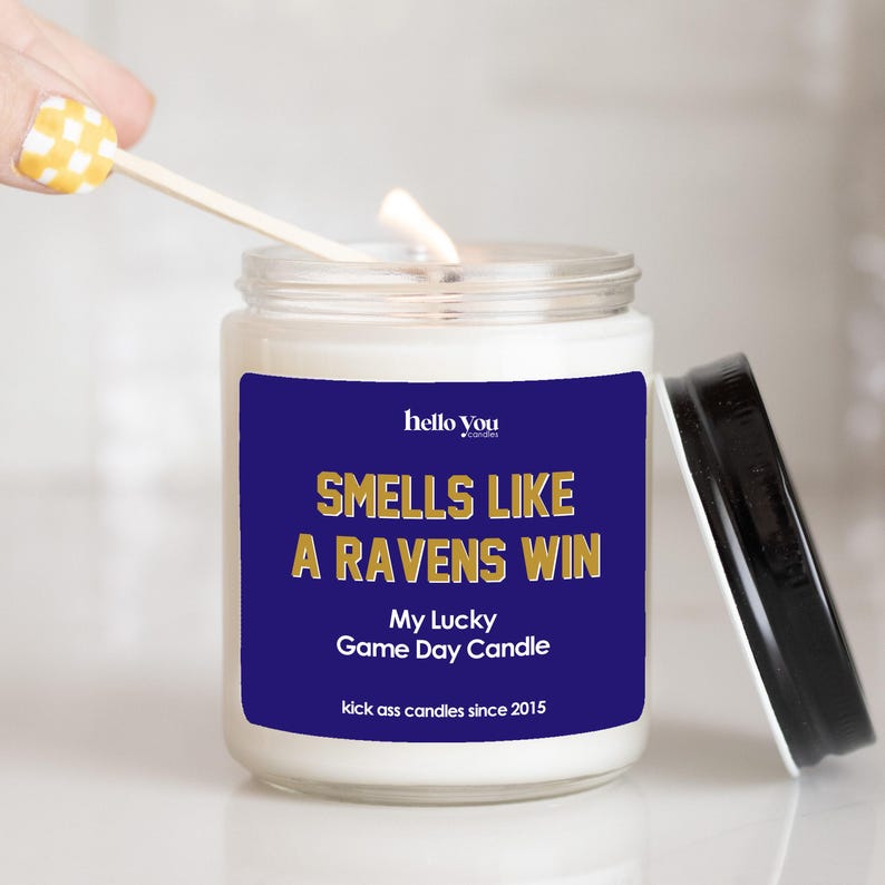 a candle labeled "SMIELS LIKE A RAVENS WIN My Lucky Game Day Candle" with a yellow and white checkered spoon sticking out of it.