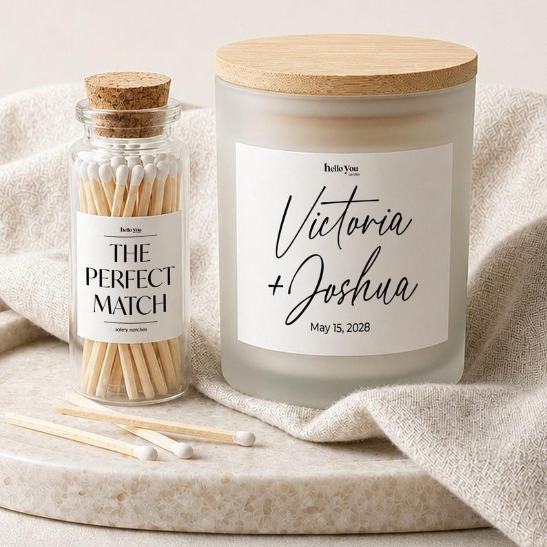 a candle labeled "Victoria + Joshua May 15, 2028" and a matchbox filled with white matchsticks, both placed on a beige cloth.