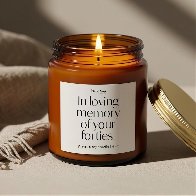 A brown soy candle with a lit flame, placed on a beige surface next to a gold-colored lid.