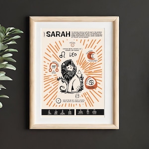 Op de afbeelding: Een ingelijste astrologische print met de naam Sarah, een centrale zwarte leeuwillustratie en diverse sterrenbeelden waaronder Leeuw, Noordknoop, Maan en Ascendant. Het ontwerp bevat oranje zonnestralen op een crèmekleurige achtergrond met tekst.