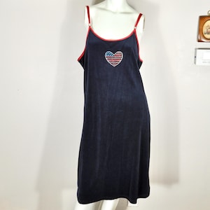 Puede incluir: Vestido lencero azul marino con ribete y tirantes rojos. El vestido presenta un diseño en forma de corazón con un patrón de bandera americana en la parte delantera. El vestido se exhibe en un maniquí.
