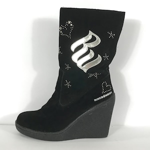 May include: Black suede wedge boot with silver accents. The boot features a large silver letter "R" and small heart and star-shaped rhinestones. The brand name "ROCAWEAR" is printed on the side.