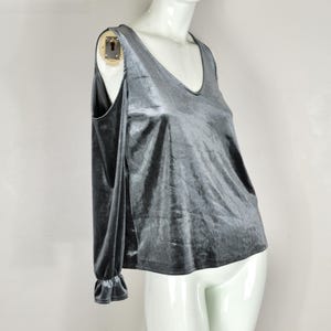 May include: A gray velvet top with a V-neck and long sleeves. The sleeves have a cold shoulder design and end in a ruffled cuff. The top is displayed on a white mannequin.