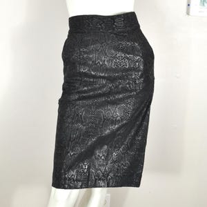 May include: A black pencil skirt with a snakeskin pattern. The skirt is knee-length and has a high waist. The fabric has a textured appearance, and the skirt is displayed on a mannequin.