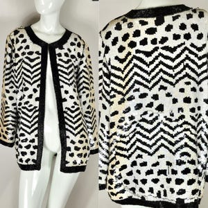 May include: A black and white sequined jacket with a distinctive pattern. The open-front jacket has black trim and a combination of chevron and polka dot designs. The sleeves are three-quarter length, and the jacket is displayed on a mannequin.