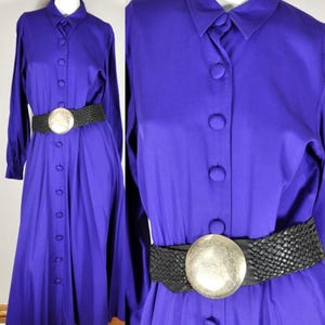 May include: A long, button-down, purple dress with long sleeves and a black woven belt. The belt has a large, round, silver-colored buckle. The dress is displayed on a mannequin.