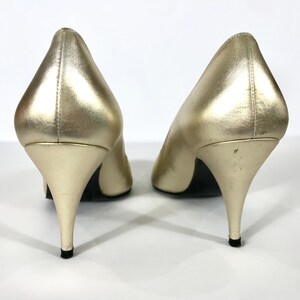 May include: A pair of gold-colored high heels with pointed toes and stiletto heels. The shoes have a metallic sheen and are set against a white background. The heels are approximately 3 inches tall.