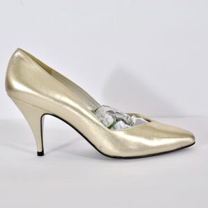 May include: Gold-colored high-heeled shoe with a pointed toe. The heel is slender and black-tipped. The shoe is filled with white paper. The shoe is likely made of leather or a similar material.