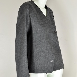 May include: A gray blazer with a V-neck and two dark buttons. The jacket is displayed on a white mannequin. The fabric has a subtle vertical stripe pattern. The blazer has long sleeves.