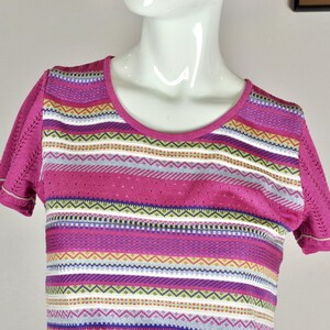 May include: A pink short-sleeved shirt with a colorful striped pattern. The stripes are a mix of pink, white, gray, blue, green, and yellow.