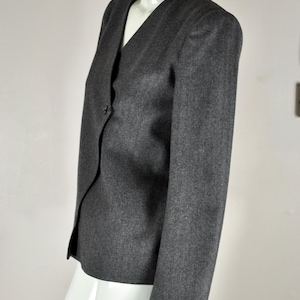 May include: A gray blazer with a V-neck and a single button closure. The jacket has long sleeves and a tailored fit. The fabric appears to be a wool blend. The blazer is displayed on a white mannequin.