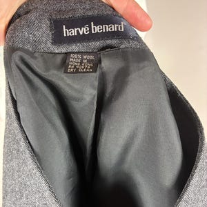 May include: Close-up of a gray wool blazer interior. The label reads "harv&eacute; benard" in white text on a black background. The tag states "100% wool, made in Hong Kong, RN 40679, dry clean."