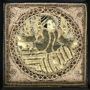 May include: A framed embroidered artwork depicting a figure in a colorful, patterned garment. The artwork is surrounded by a decorative border of beads and embroidery.