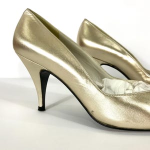 May include: A pair of gold-colored high heels with pointed toes and stiletto heels. The shoes have a metallic sheen and a classic design, suitable for formal occasions. The heels are approximately 3 inches high.