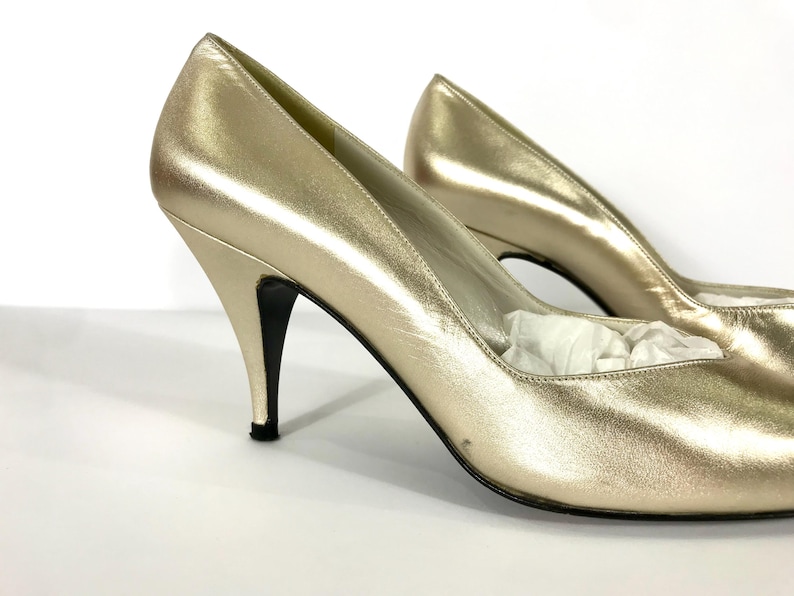 May include: A pair of gold-colored high heels with pointed toes and stiletto heels. The shoes have a metallic sheen and a classic design, suitable for formal occasions. The heels are approximately 3 inches high.