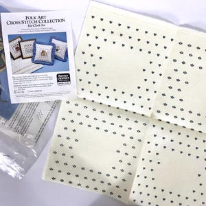 Op de afbeelding: Een kruissteekset met drie kleine kussenontwerpen. De set bevat Aida-stof, borduurzijde en instructies. De set is uit de Folk Art Cross-Stitch Collection van Better Homes and Gardens.